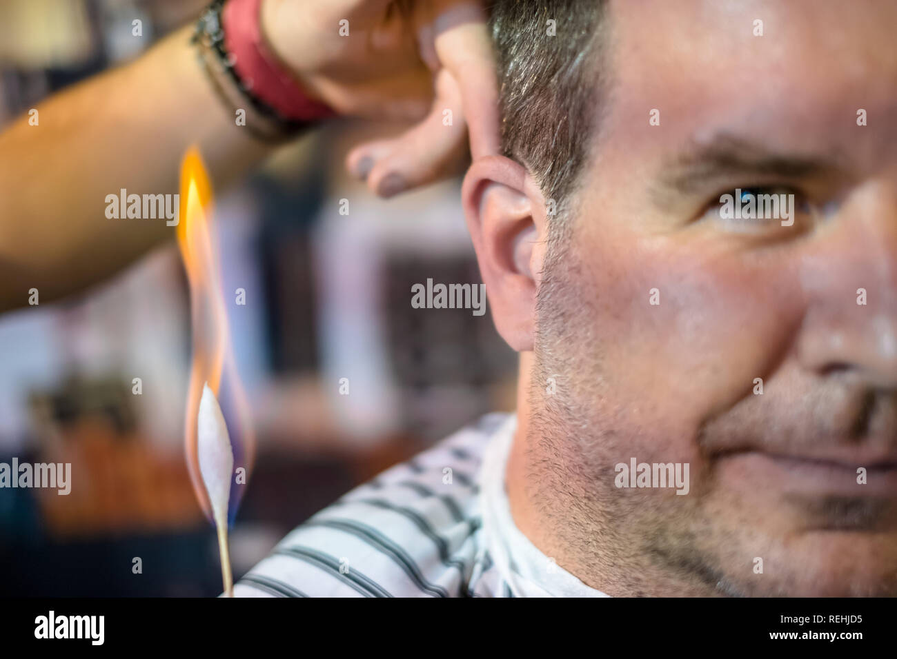 Un salon de coiffure est en train de brûler les petits poils à l'oreille d'un client de sexe masculin Banque D'Images