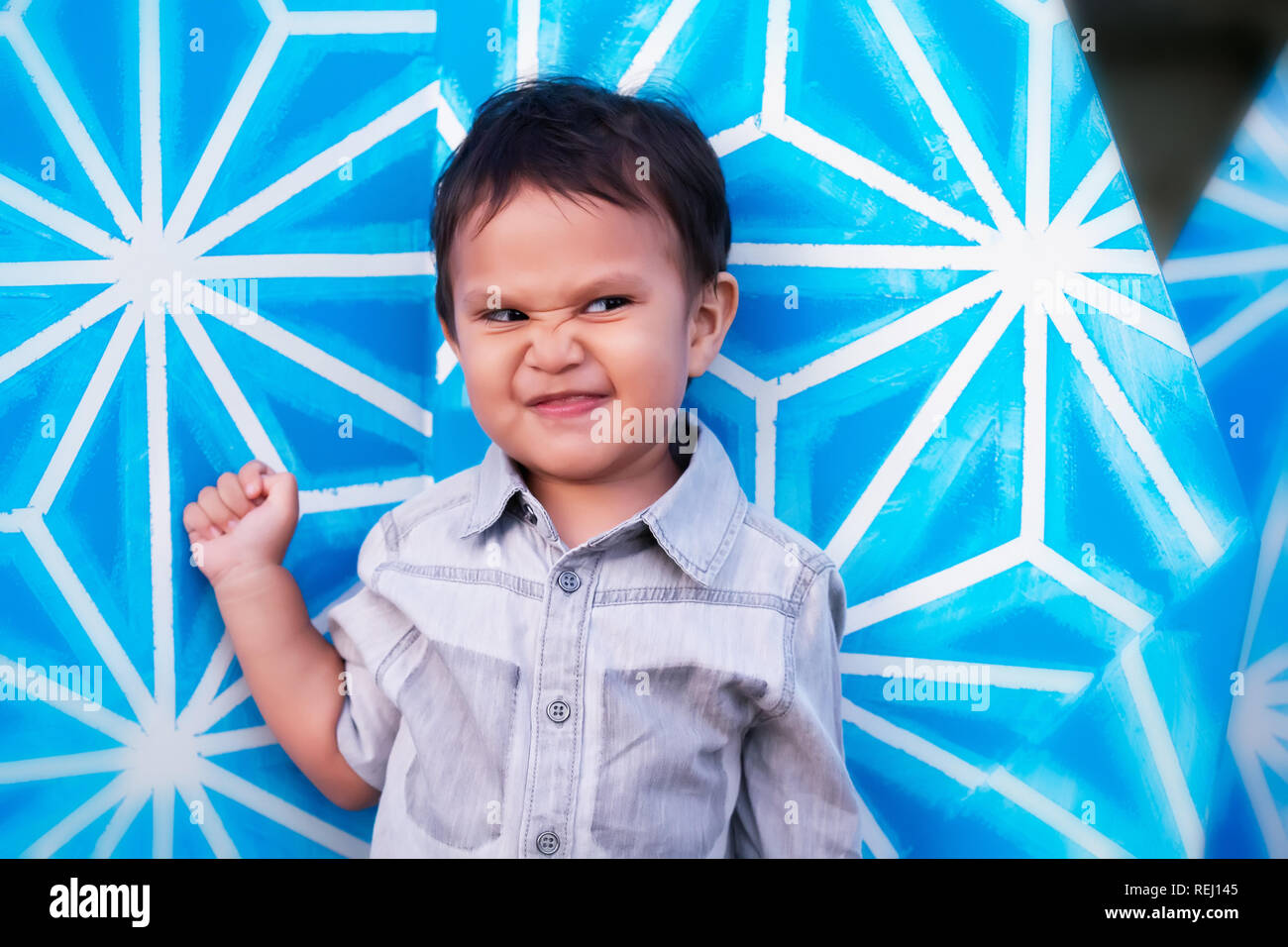 Un enfant avec plaisir l'expression moqueuse sur son visage, debout devant un fond à motifs bleu vif. Banque D'Images