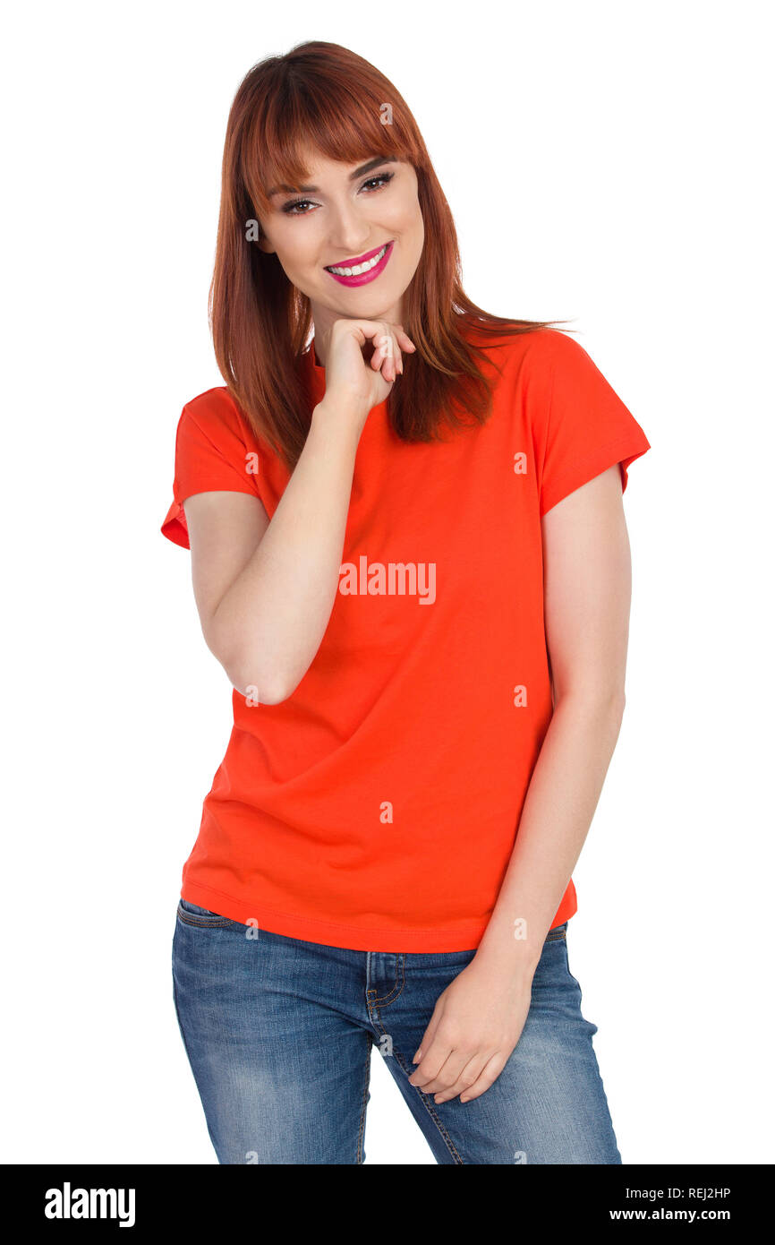 Belle jeune femme en tee-shirt orange tient la main sur le menton et sourit. Trois quarts studio shot isolé sur blanc. Banque D'Images