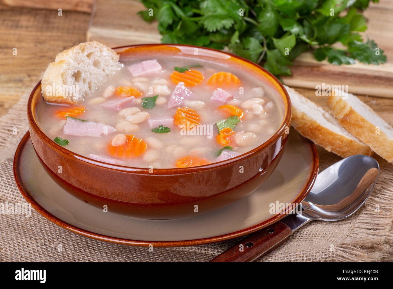 Bol de soupe aux haricots et jambon avec des carottes et du pain français Banque D'Images