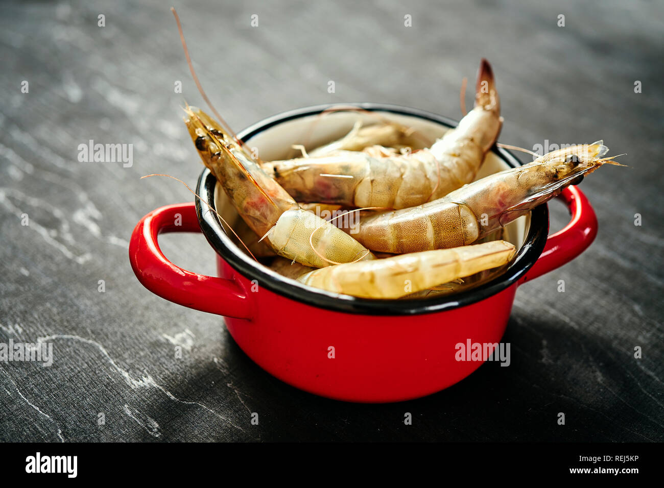 Délicieux crus frais crevettes géantes dans un pot rouge sur une table en bois noir Banque D'Images