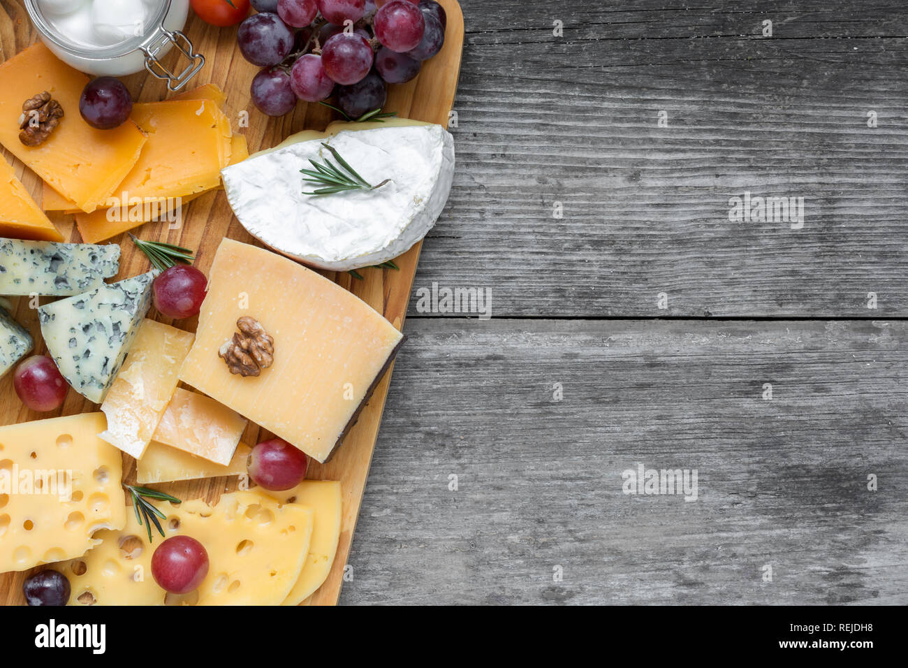Assortiment de fromages sur planche de bois plate servi avec les noix, les raisins et le romarin sur fond de bois rustique, vue supérieure avec copie espace Banque D'Images