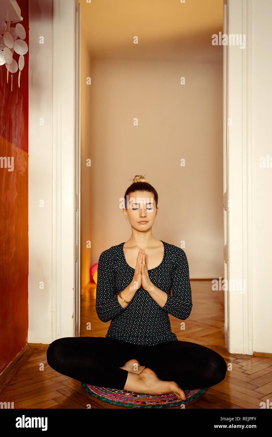 Jolie jeune femme professeur de yoga méditation assis sur un tapis sur le plancher dans un costume uni noir étant prêt pour un excellent entraînement. La tonalité de l'image. Banque D'Images