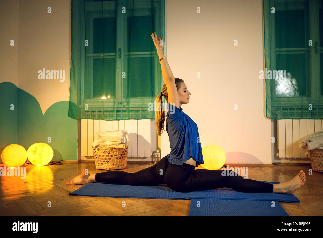 Attractive blonde woman doing yoga au cours de l'exercice partagé de la jambe en performance home studio. La tonalité de l'image. Banque D'Images