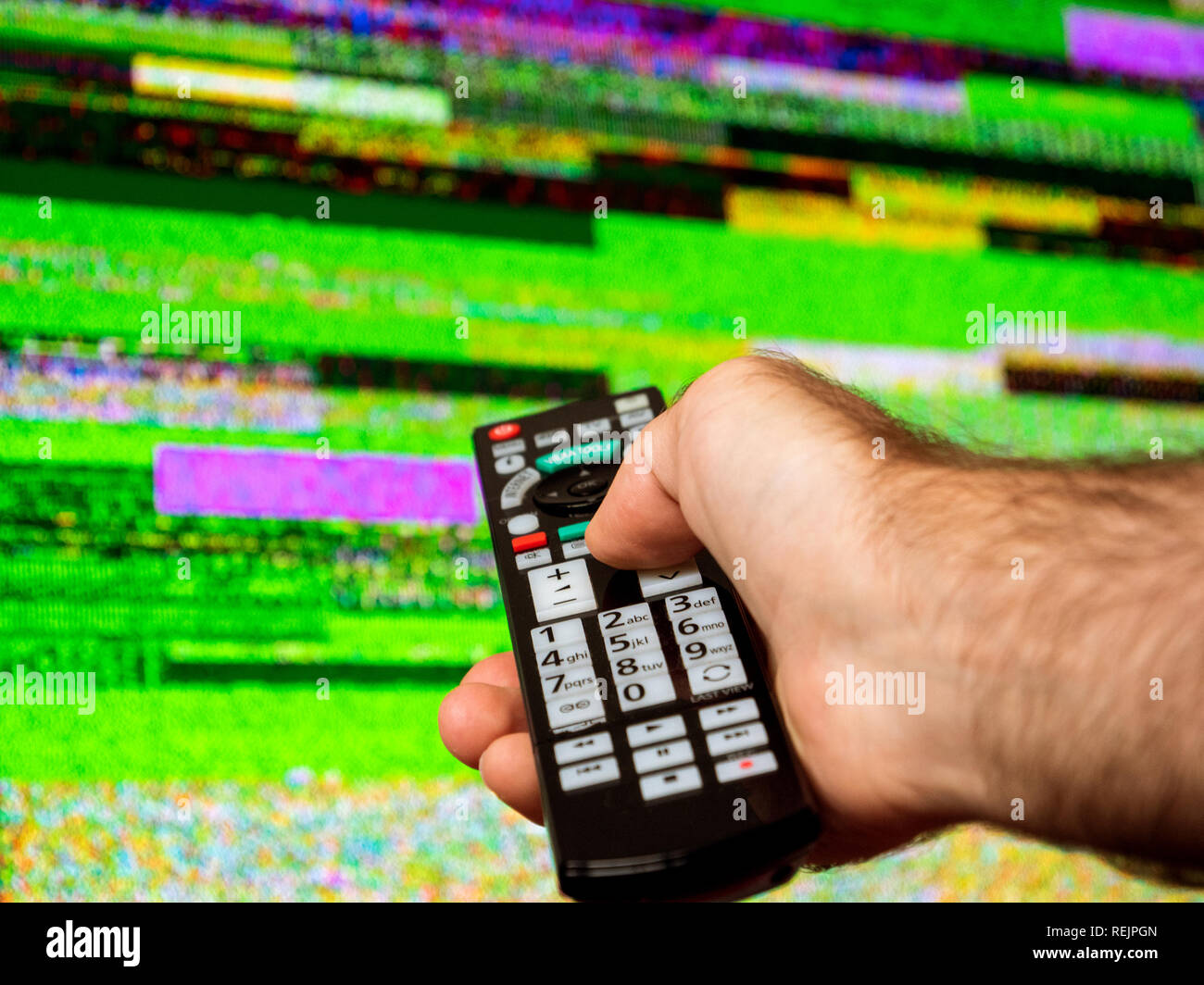 Homme avec grande télévision à essayer de réparer à distance le bruit de la télévision numérique sur un grand écran OLED plasma 4K Ultra HD High Dynamic Range HDR Smart TV . Banque D'Images