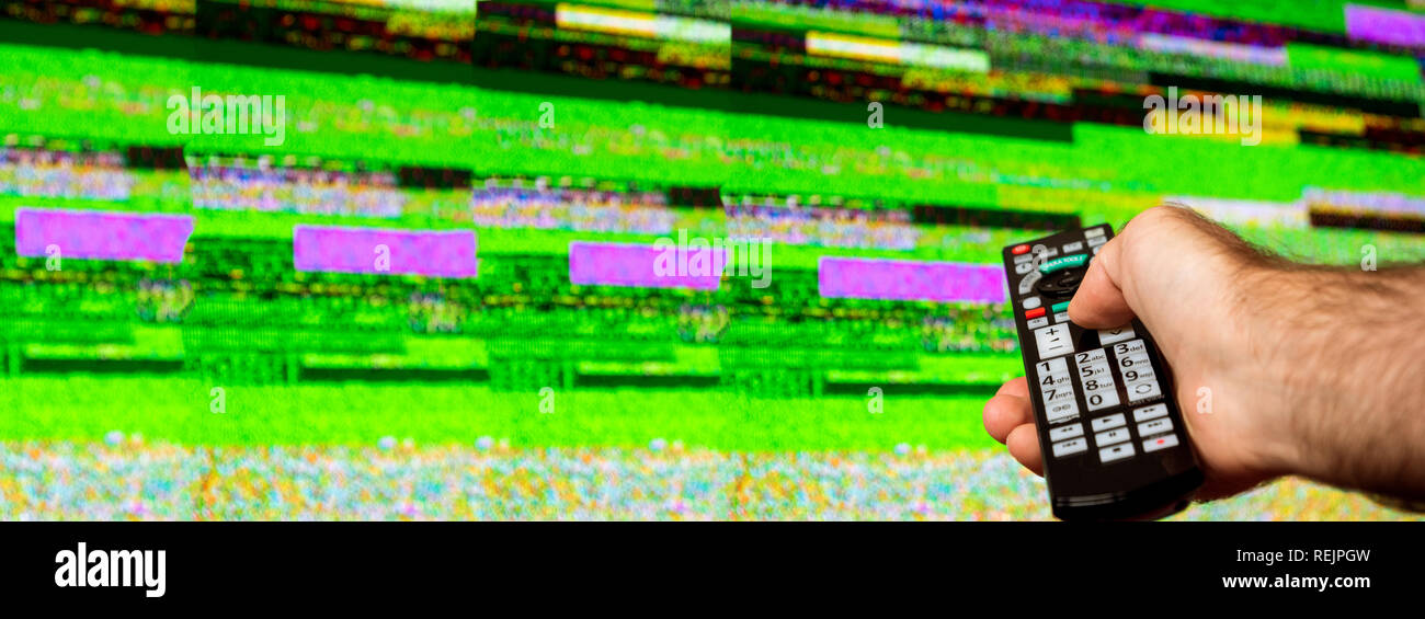 Homme avec grande télévision à essayer de réparer à distance le bruit de la télévision numérique sur un grand écran OLED plasma 4K Ultra HD High Dynamic Range HDR Smart TV . Banque D'Images