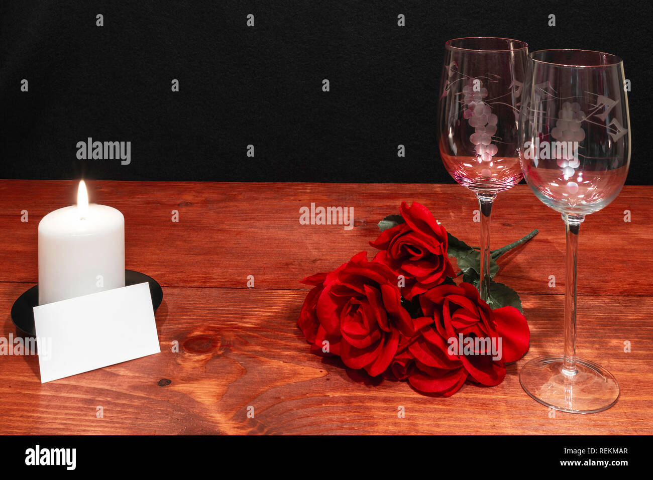 Beaux verres à vin gravés avec des roses rouges et bougie blanche sur table en bois et un arrière-plan sombre. La Saint-Valentin, fête des Mères, Pâques, Noël, Mariage Banque D'Images