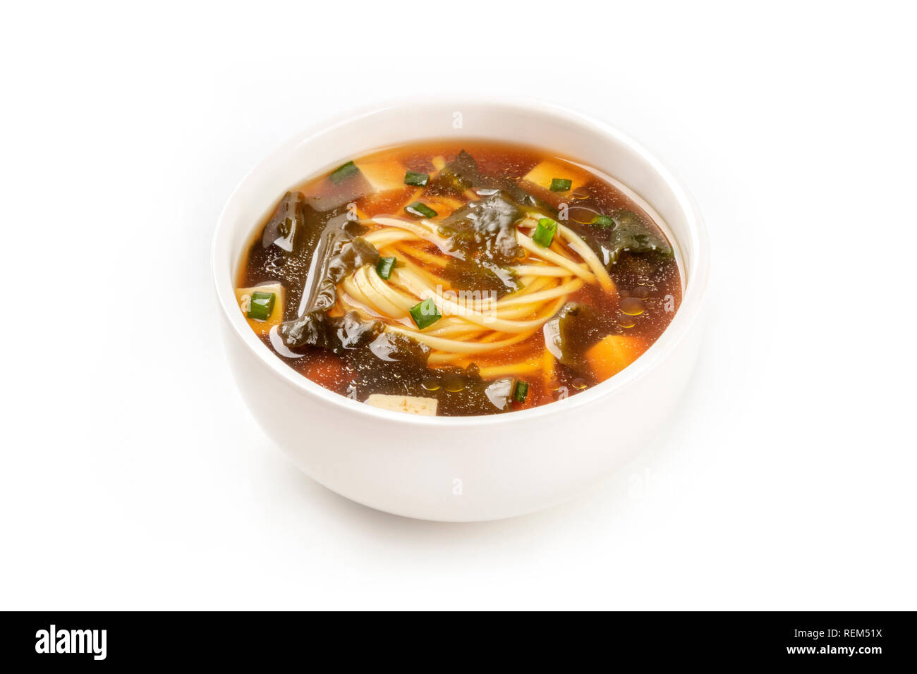 Une photo d'un bol de soupe miso avec le tofu, les oignons verts, les nouilles et les algues wakame, sur un fond blanc avec une place pour le texte Banque D'Images