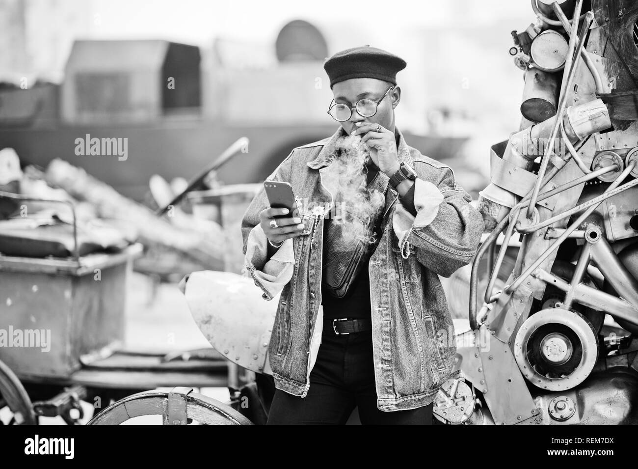 African American man veste en jeans, béret et lunettes, les fumeurs de cigare et posée contre l'ancien véhicule rétro et à la recherche au téléphone. Banque D'Images