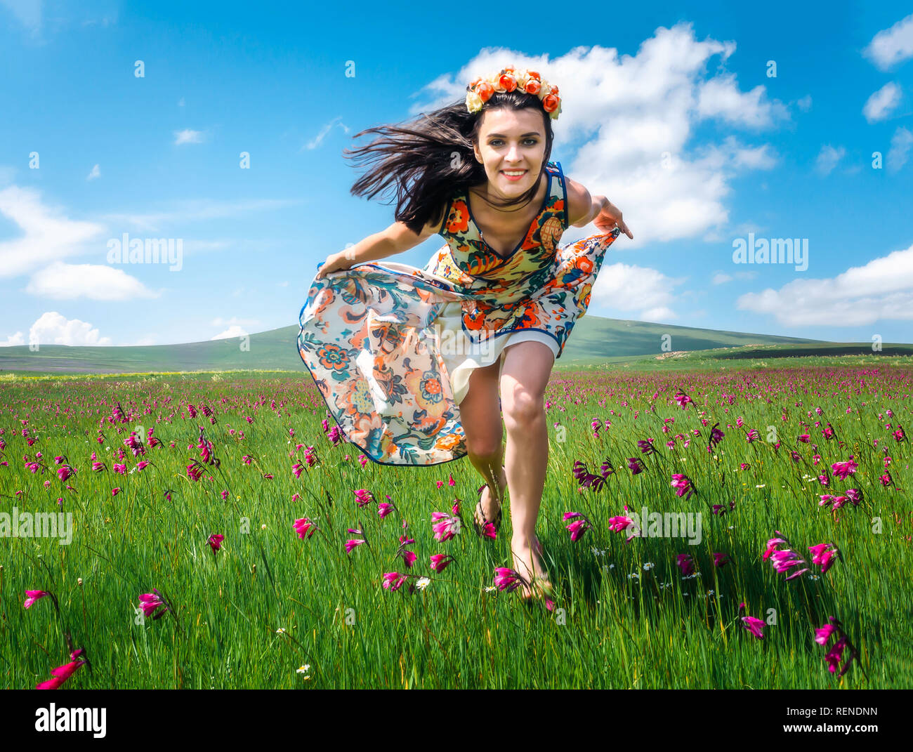 Beautiful smiling girl fonctionnant en meadom floraison en robe colorée. Jolie femme brune en guirlande le long champ. Je suis libre concept Banque D'Images