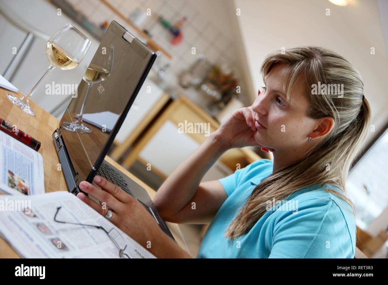 Jeune femme, de 25 à 30 ans, la navigation sur internet avec un ordinateur portable à sa table de cuisine Banque D'Images