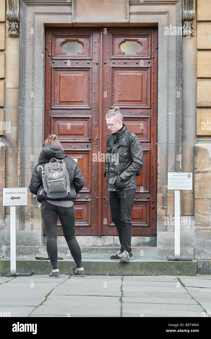 Deux visiteurs se lever et attendre à l'extérieur de l'entrée du Sheldonian Theatre à l'université d'Oxford, en Angleterre. Banque D'Images