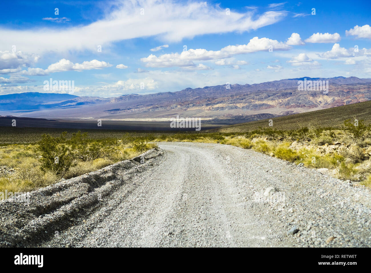 Voyageant sur une route non goudronnée à travers une région éloignée de la Death Valley National Park ; montagnes, ciel bleu et nuages blancs à l'arrière-plan ; Californie Banque D'Images