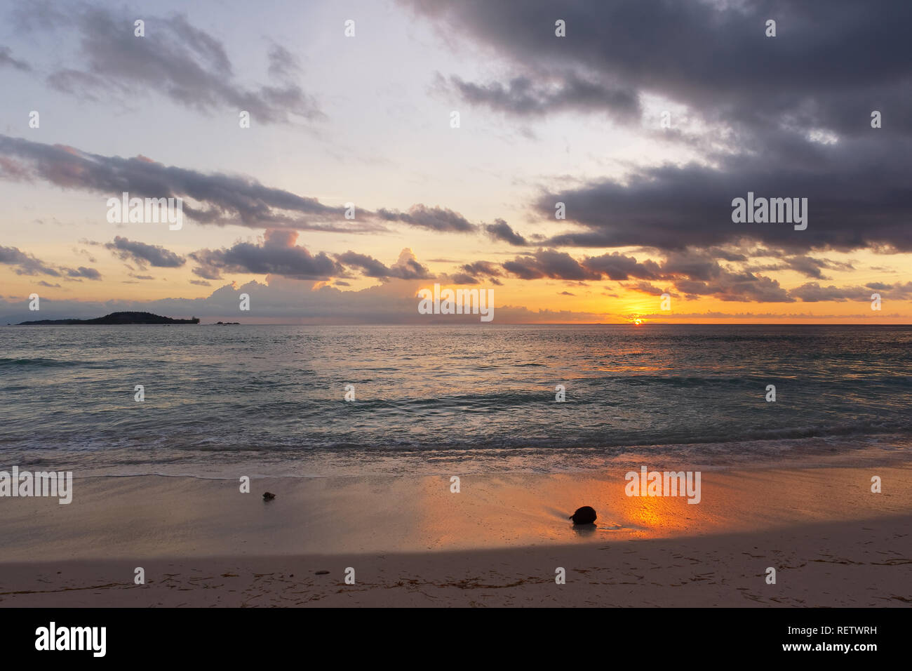 Moody de soleil colorés sur la mer, des nuages sombres s'alternent avec un ciel coloré, le soleil touche l'horizon, au premier plan sont des noix de coco sur la plage Banque D'Images