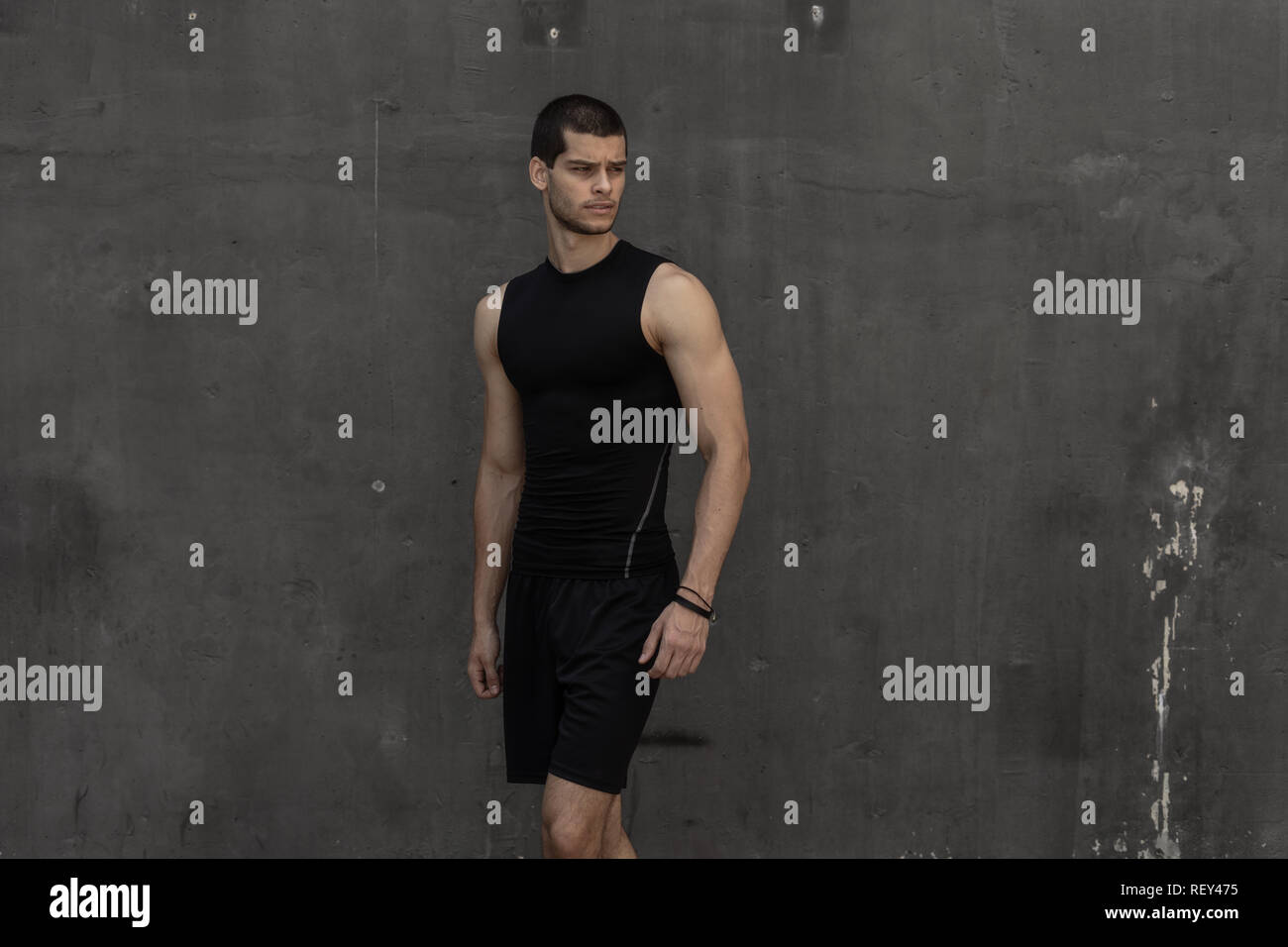 Portrait de jeune homme musclé athlétique, dans les vêtements de sport, posant sur l'arrière-plan industriel gris. Hauteur à la mode homme, un modèle sportif, corps musclé s Banque D'Images
