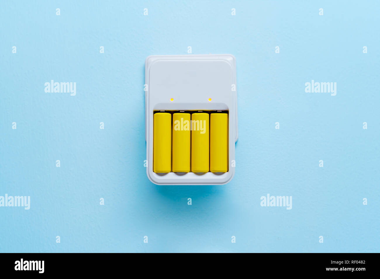 Photo de chargeur avec piles jaunes sur fond bleu vide Banque D'Images
