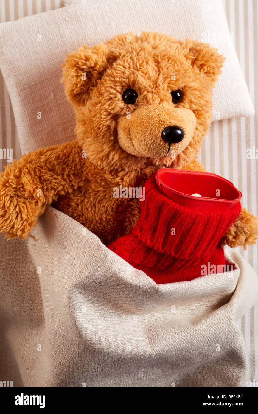 Petit ours malade au lit avec une bouteille d'eau chaude dans une couverture en tricot rouge coloré dans un concept de soins pédiatriques Banque D'Images