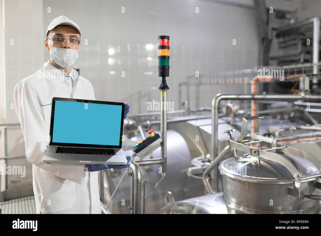 Homme d'une robe blanche et un masque avec un ordinateur portable dans ses mains est à l'usine Banque D'Images