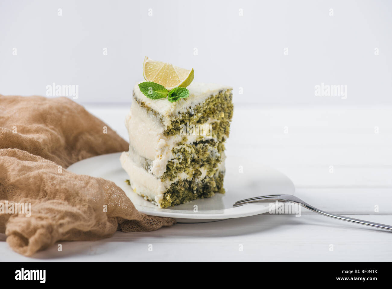 Morceau de gâteau blanc décoré d'une tranche de lime et de menthe congé avec fourche de soucoupe isolated on white Banque D'Images