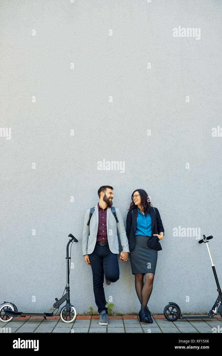 Couple heureux avec des scooters appuyé contre un mur Banque D'Images