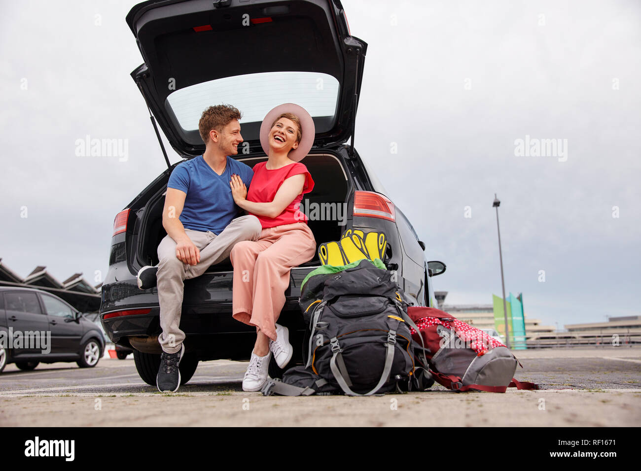 Happy young couple sitting in car boot à l'aéroport Banque D'Images