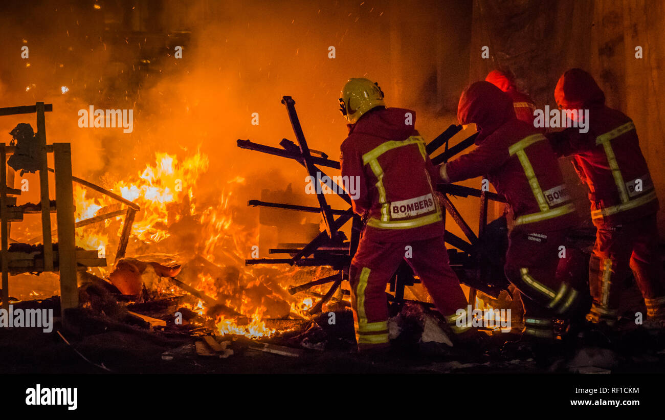 Les Pompiers au travail en uniforme en de de l'incendie en mettant les restes d'une falla sculpture en papier à Las Fallas festival à Cullera, Valenci Banque D'Images