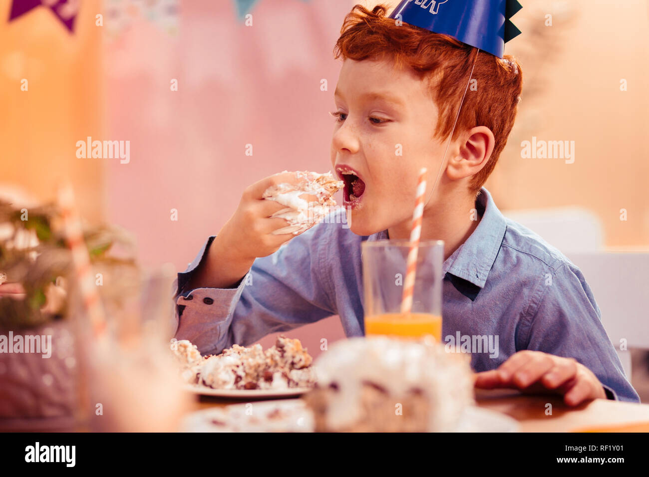 Garçon aux cheveux rouge faim manger délicieux gâteau d'anniversaire Banque D'Images