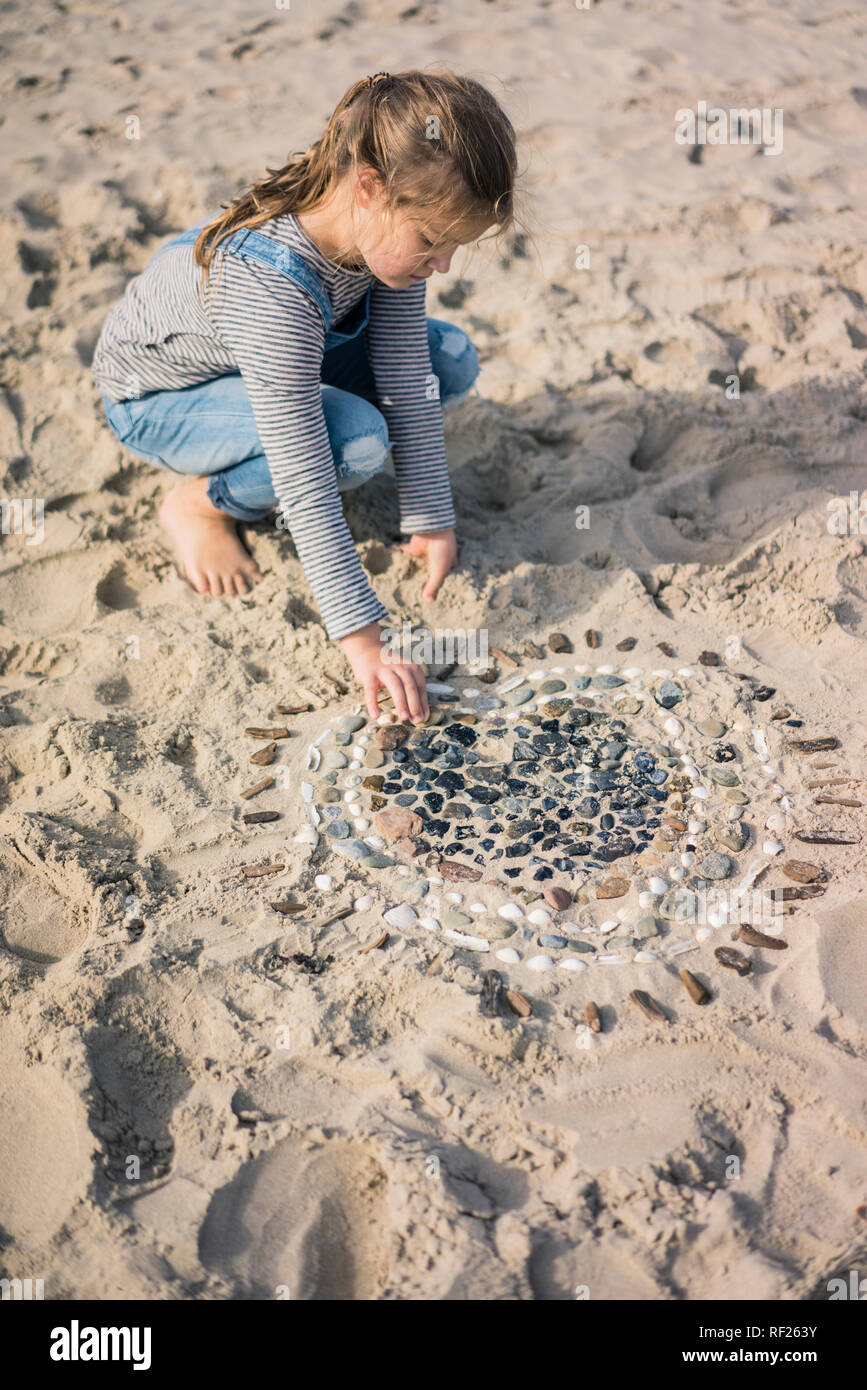 Petite fille faisant un coeur de coquillages sur la plage Banque D'Images