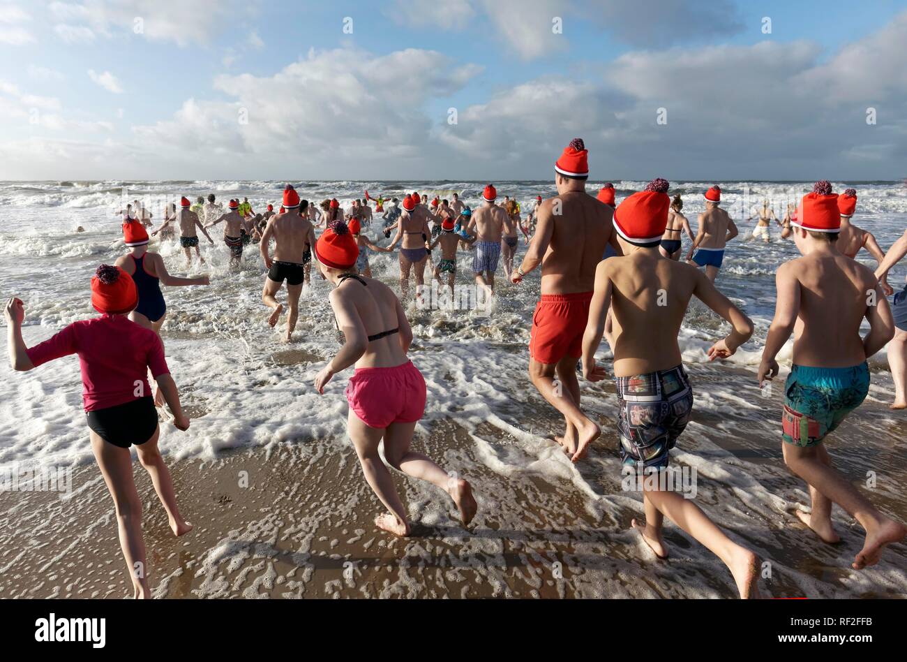 Beaucoup de gens en maillots de bain et de chapeaux de Noël courir dans la mer froide en hiver, la nouvelle année natation, Mer du Nord, Bergen aan Zee Banque D'Images