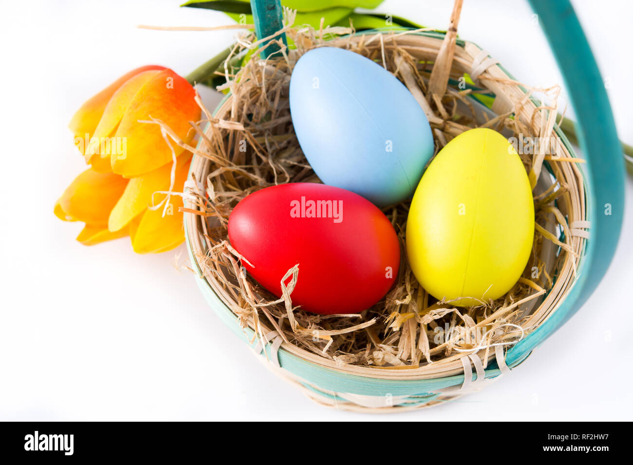 Les oeufs de Pâques colorés dans un panier et tulipes isolé sur fond blanc. Banque D'Images