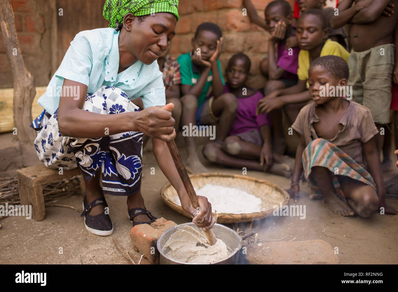 Une femme du Malawi s'agite nsima cuit sur un feu ouvert au cours d'une visite communautaire pour les touristes à Majete Wildlife Reserve ; elle décrit les étapes. Banque D'Images