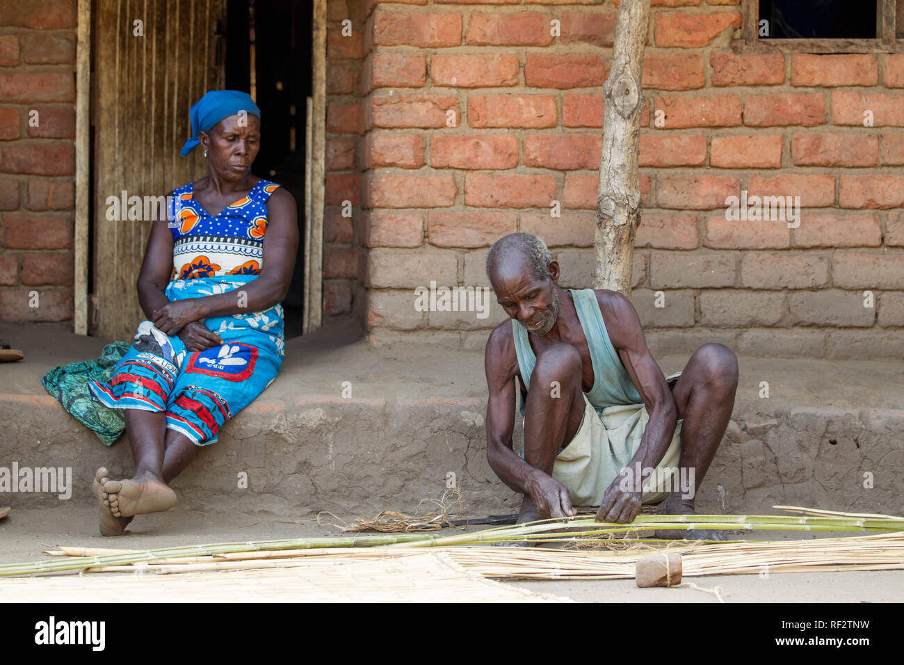 Un homme tisse un tapis de roseaux en utilisant la technique traditionnelle dans un village de Chikwawa, Malawi comme sa femme regarde. Banque D'Images