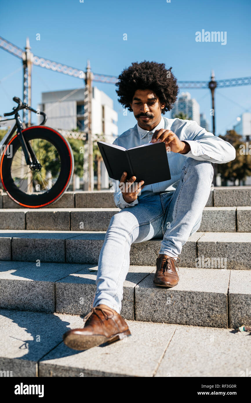 Mid adult man avec location assis sur des escaliers, dans un livre de lecture Banque D'Images