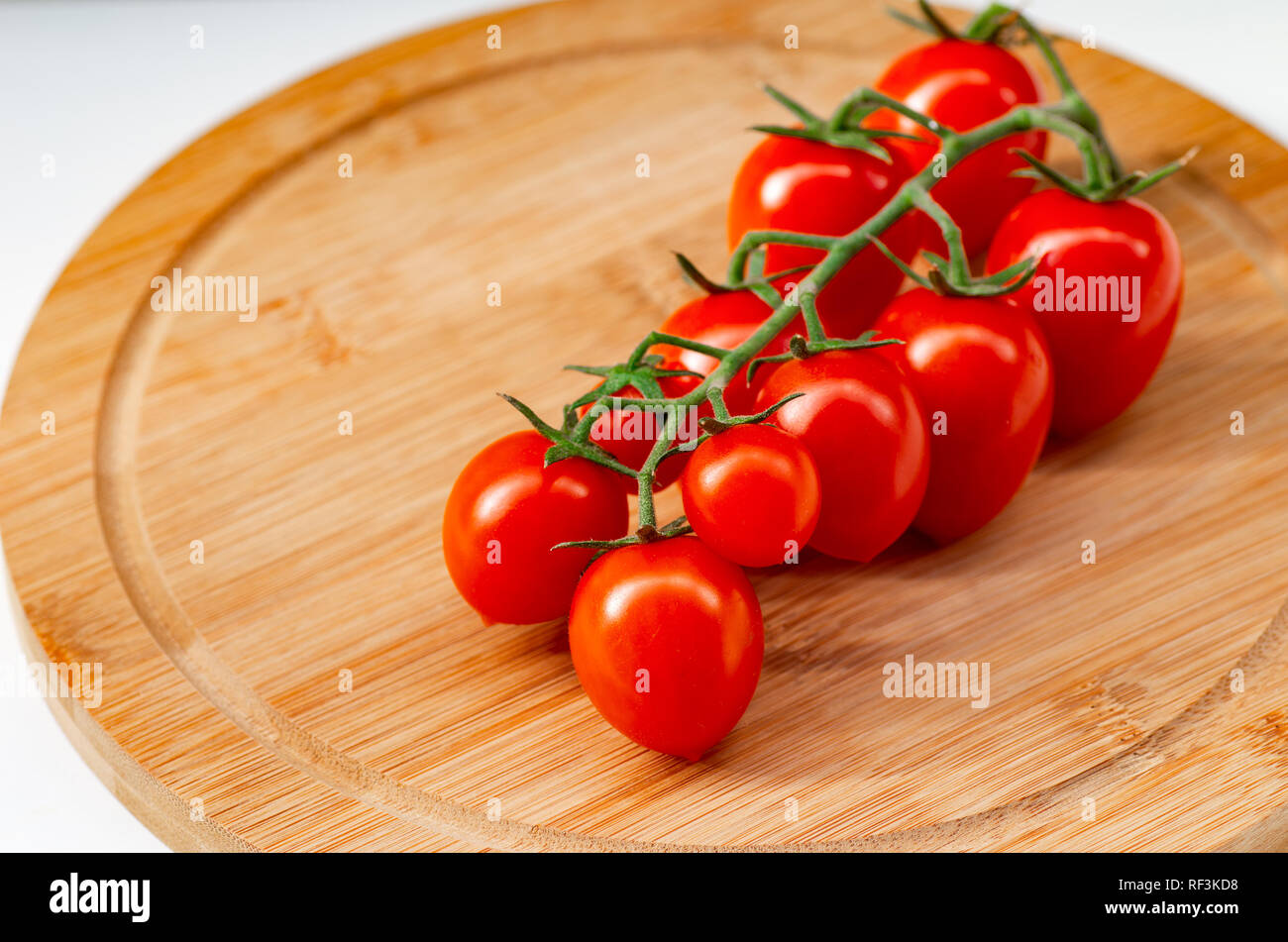 La branche de tomates cerise sur un fond de bois. Les tomates cerise et les feuilles de basilic sur un fond blanc. Banque D'Images