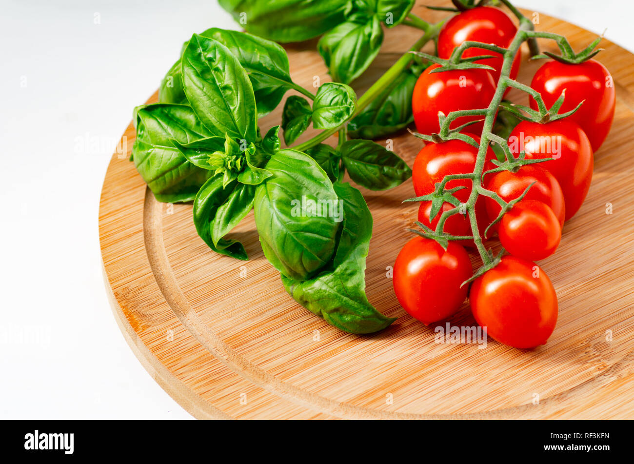 La branche de tomates cerise sur un fond de bois. Les tomates cerise et les feuilles de basilic sur un fond blanc. Banque D'Images