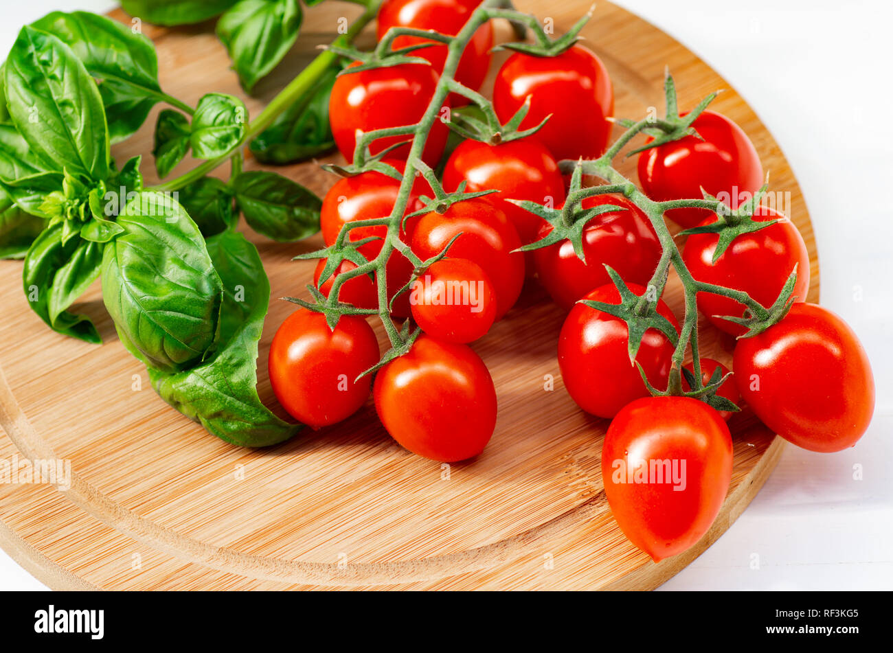 La branche de tomates cerise sur un fond de bois. Les tomates cerise et les feuilles de basilic sur un fond blanc. Banque D'Images