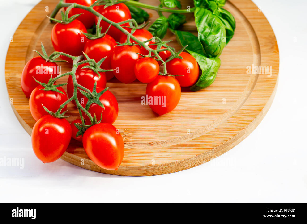 La branche de tomates cerise sur un fond de bois. Les tomates cerise et les feuilles de basilic sur un fond blanc. Banque D'Images
