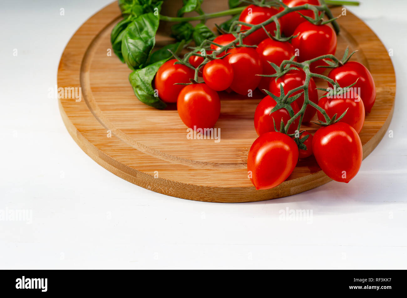 La branche de tomates cerise sur un fond de bois. Les tomates cerise et les feuilles de basilic sur un fond blanc. Banque D'Images