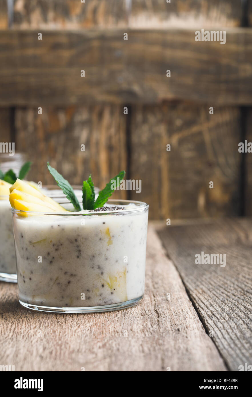 Smoothie banane mangue en verre, dessert sain naturel avec du yaourt grec et chia seeds, petit déjeuner végétarien avec du miel sur la table en bois, clos rural Banque D'Images