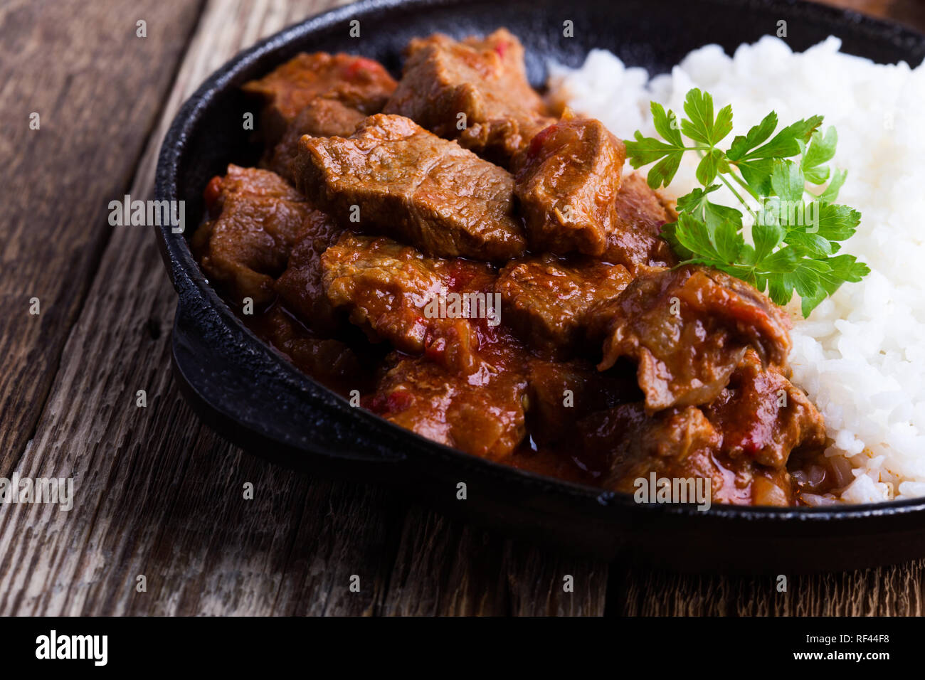 Ragoût de boeuf servi avec du riz blanc dans la poêle en fonte sur table en bois rustique, close-up, selective focus Banque D'Images