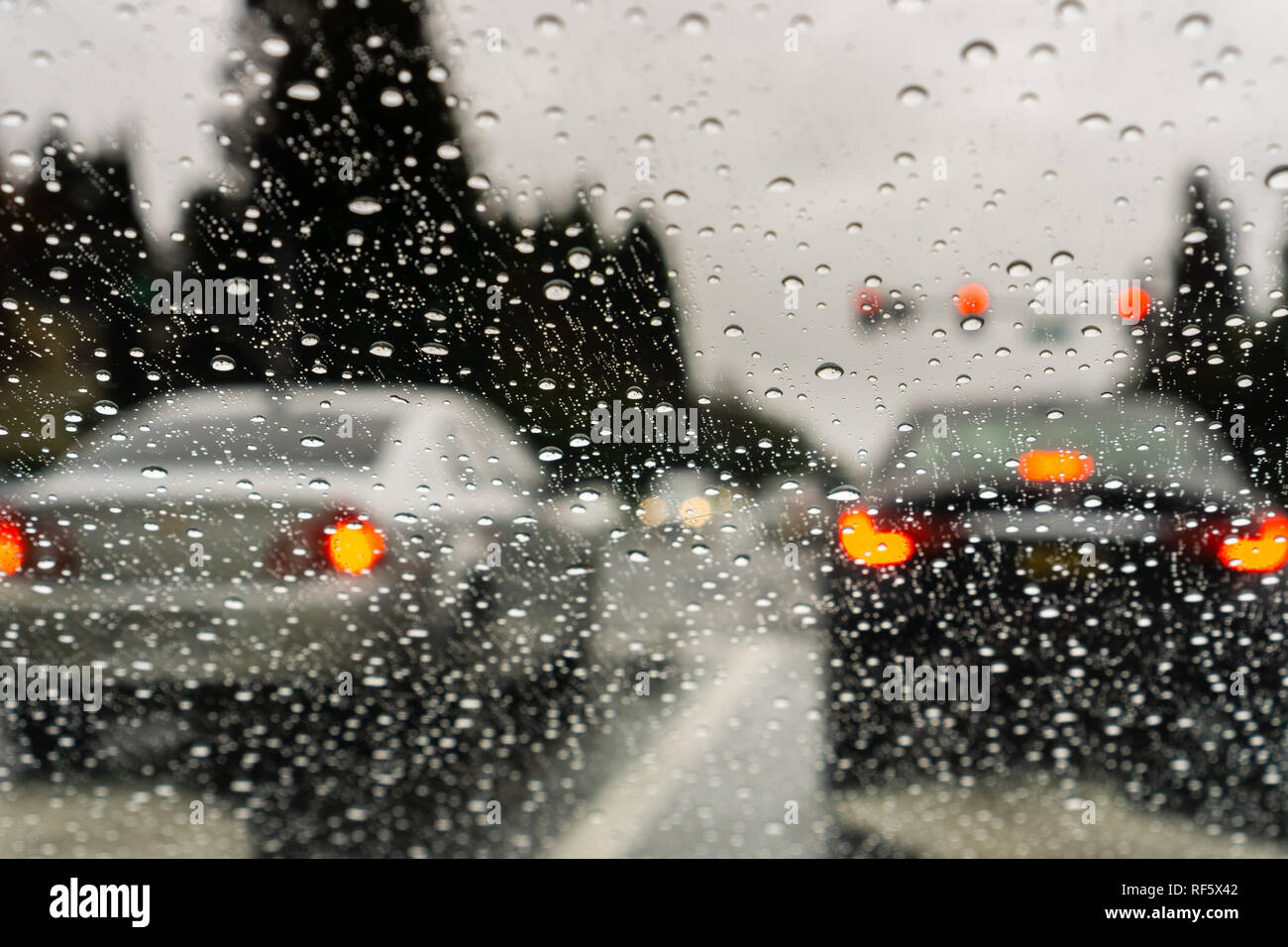 Gouttes de pluie sur le pare-brise un jour de pluie ; voitures arrêtées à un feu rouge à l'arrière-plan ; Californie Banque D'Images