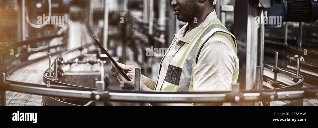 Employé d'usine à l'aide d'une tablette numérique près de la ligne de production Banque D'Images