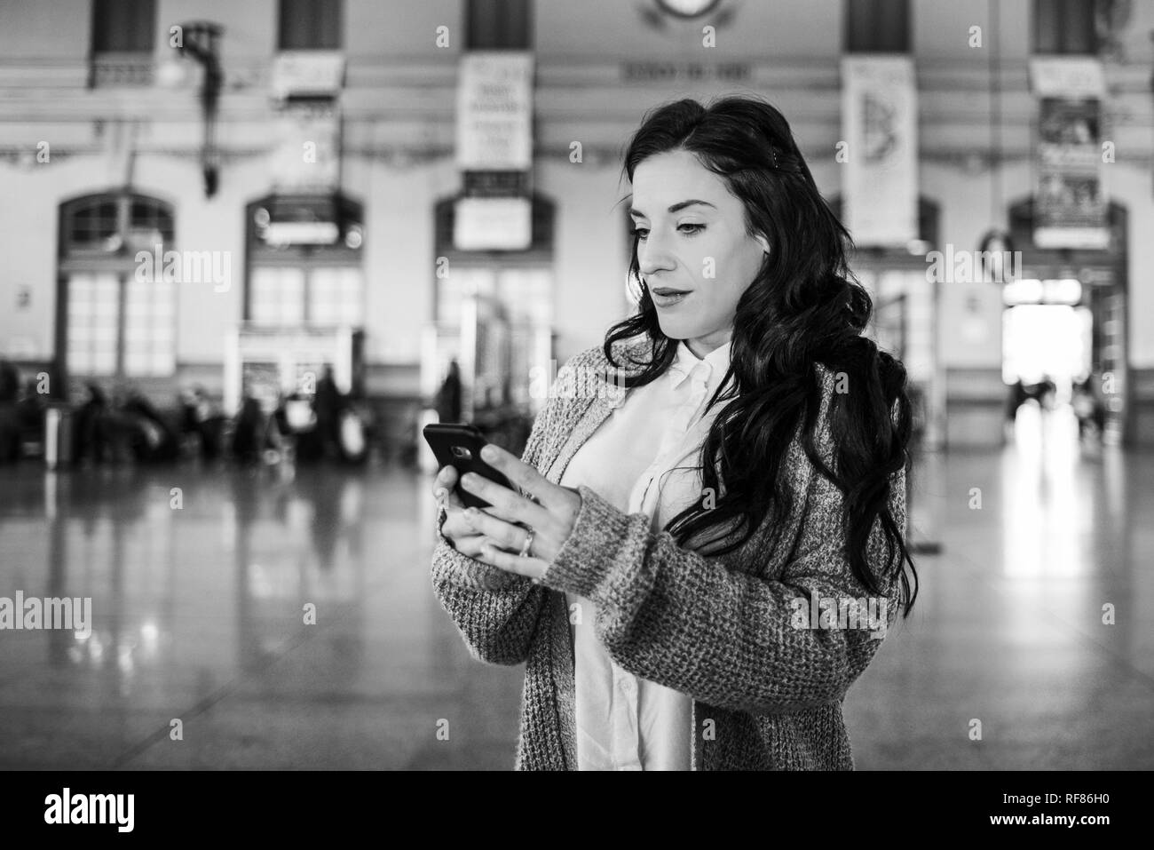 Belle femme mature contrôler les horaires de train sur son téléphone mobile, photo en blanck et blanc. Banque D'Images