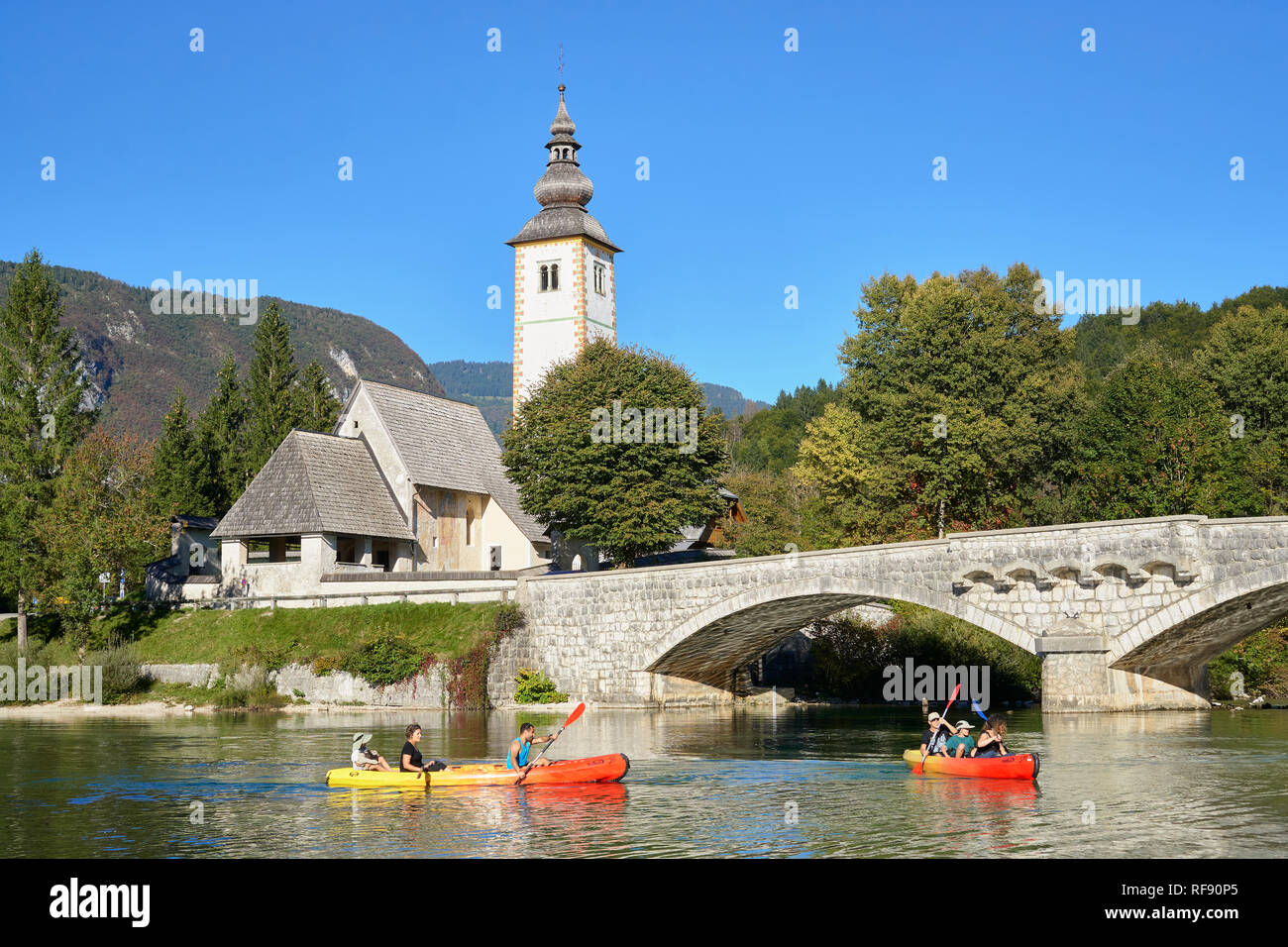 L'église de St Jean le Baptiste, Cerkev Sv. Janeza Krstnika, et le lac de Bohinj, Bohinj, Ribcev Laz, Haute-Carniole, la Slovénie. Avec les canoéistes sur le lac Banque D'Images