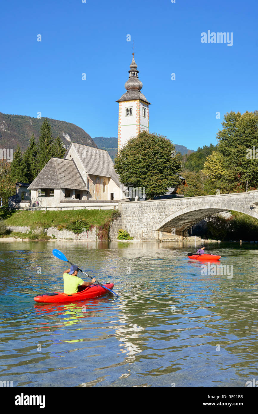 L'église de St Jean le Baptiste, Cerkev Sv. Janeza Krstnika, et le lac de Bohinj, Bohinj, Ribcev Laz, Haute-Carniole, la Slovénie. Avec les canoéistes sur le lac Banque D'Images