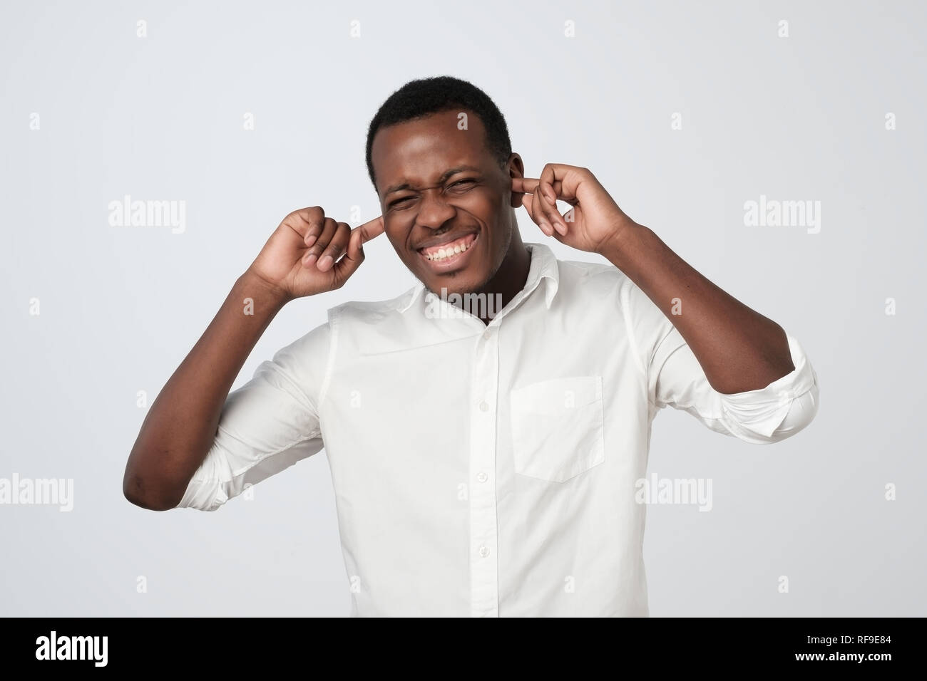 Cheerful african man in white shirt boucher les oreilles avec les doigts et avec un clin. Banque D'Images