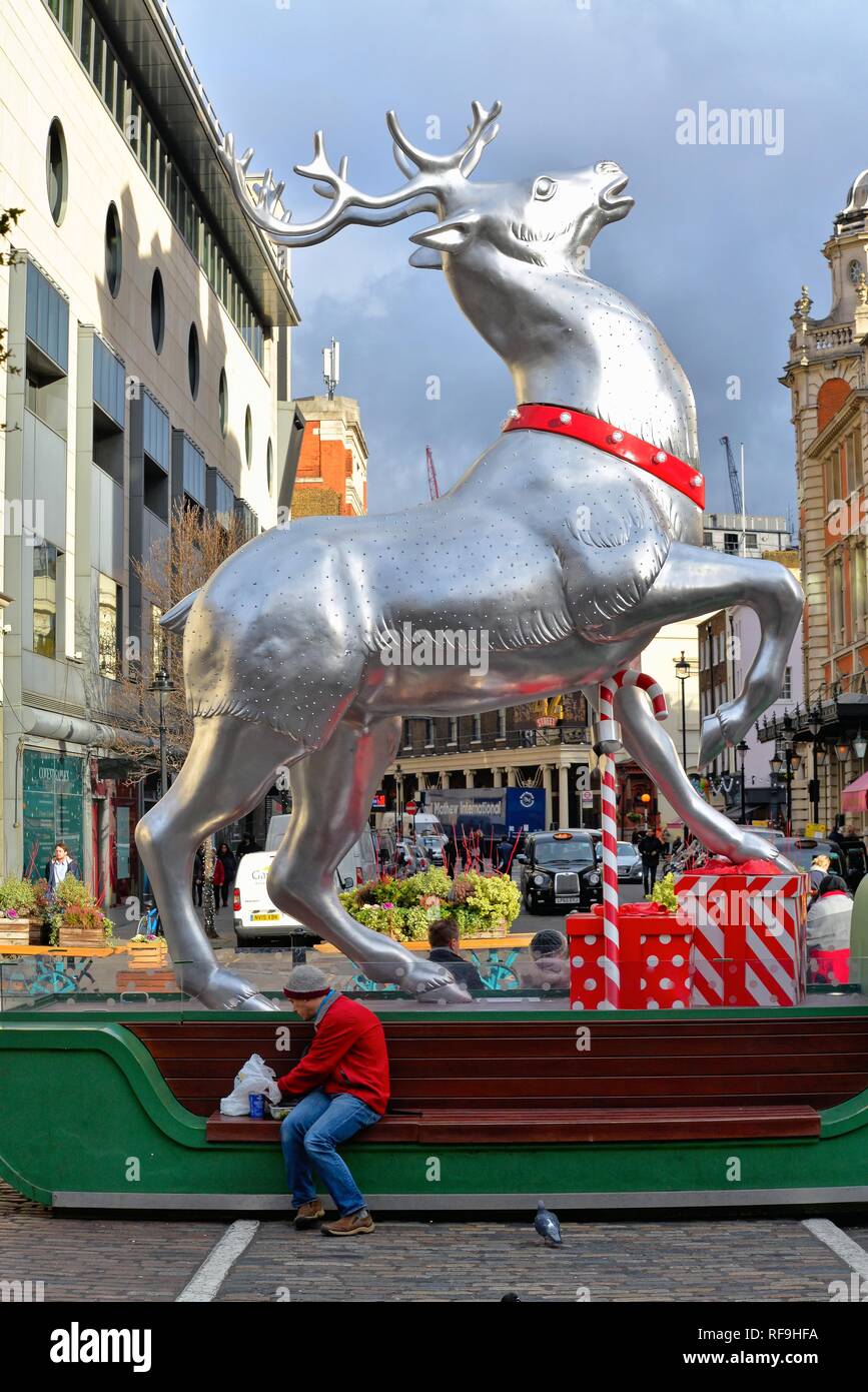 Un jeune homme assis sous un géant de l'alimentation des rennes d'argent Décorées pour Noël dans jardin du couvent Central London England UK Banque D'Images