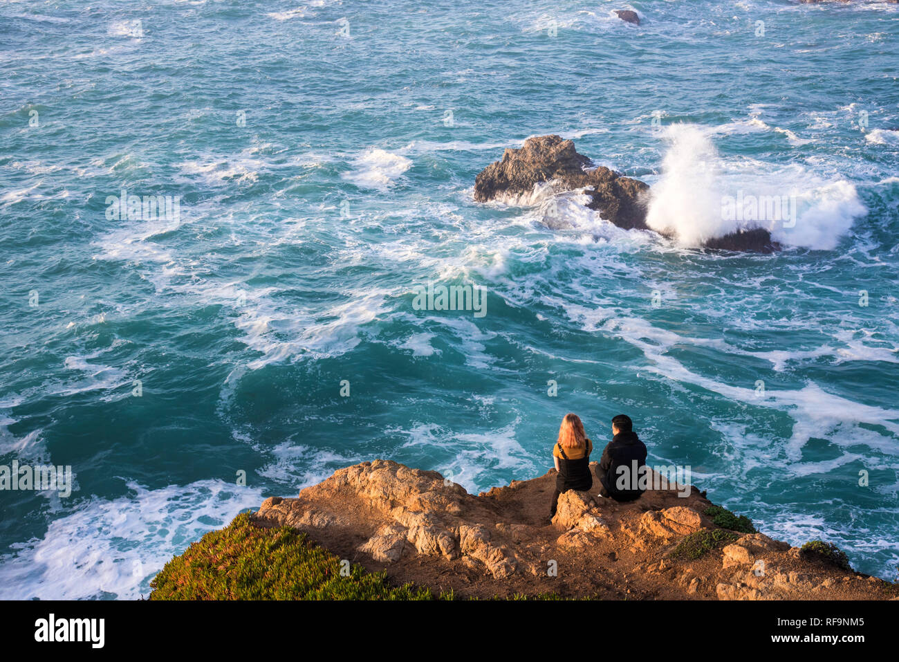 Un jeune couple qui regarde les vagues puissantes s'écraser sur le rivage. Banque D'Images