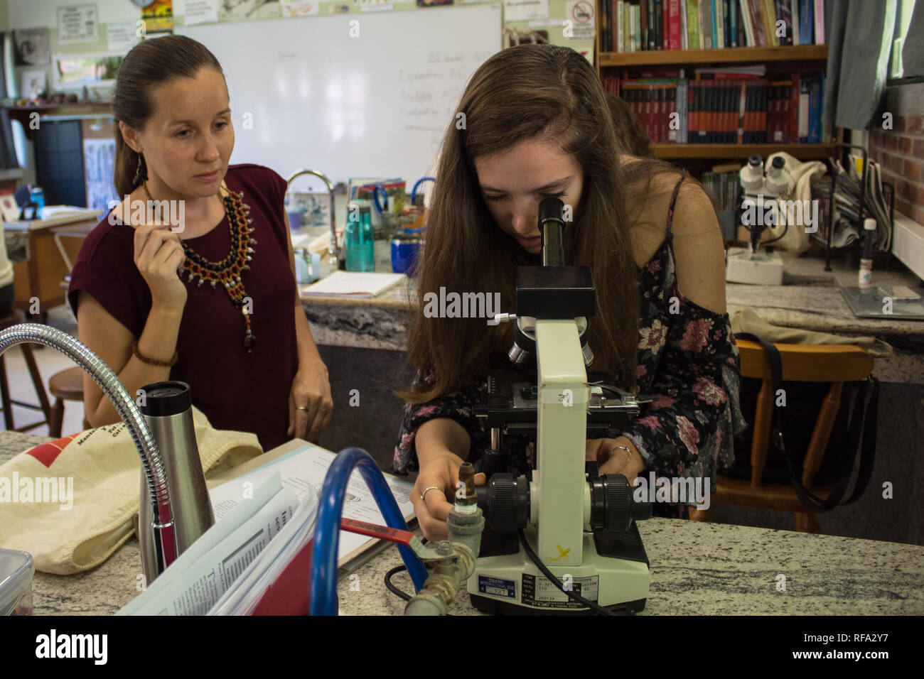 Une femme professeur de biologie l'observation d'un étudiant international à la recherche d'un microscope par classe de sciences. Banque D'Images