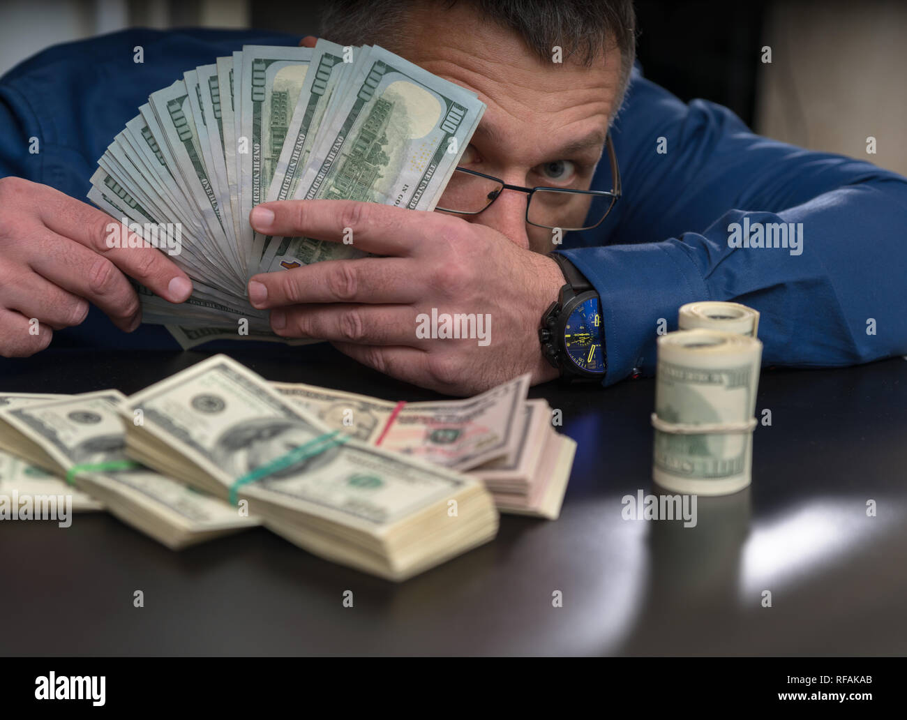 Businessman, joueur ou officiel corrompu portant des lunettes sur le site de derrière une poignée d'argent avec des paquets de 100 dollar bills en face de lui Banque D'Images